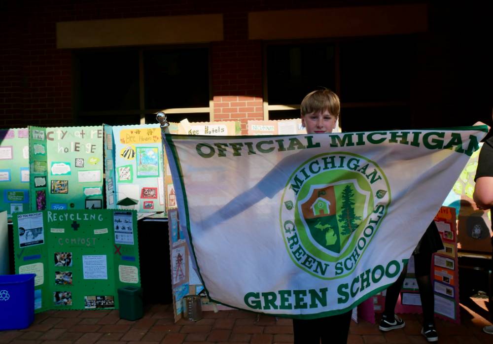 Student holds up "Official Michigan Green School" flag in front of school posters